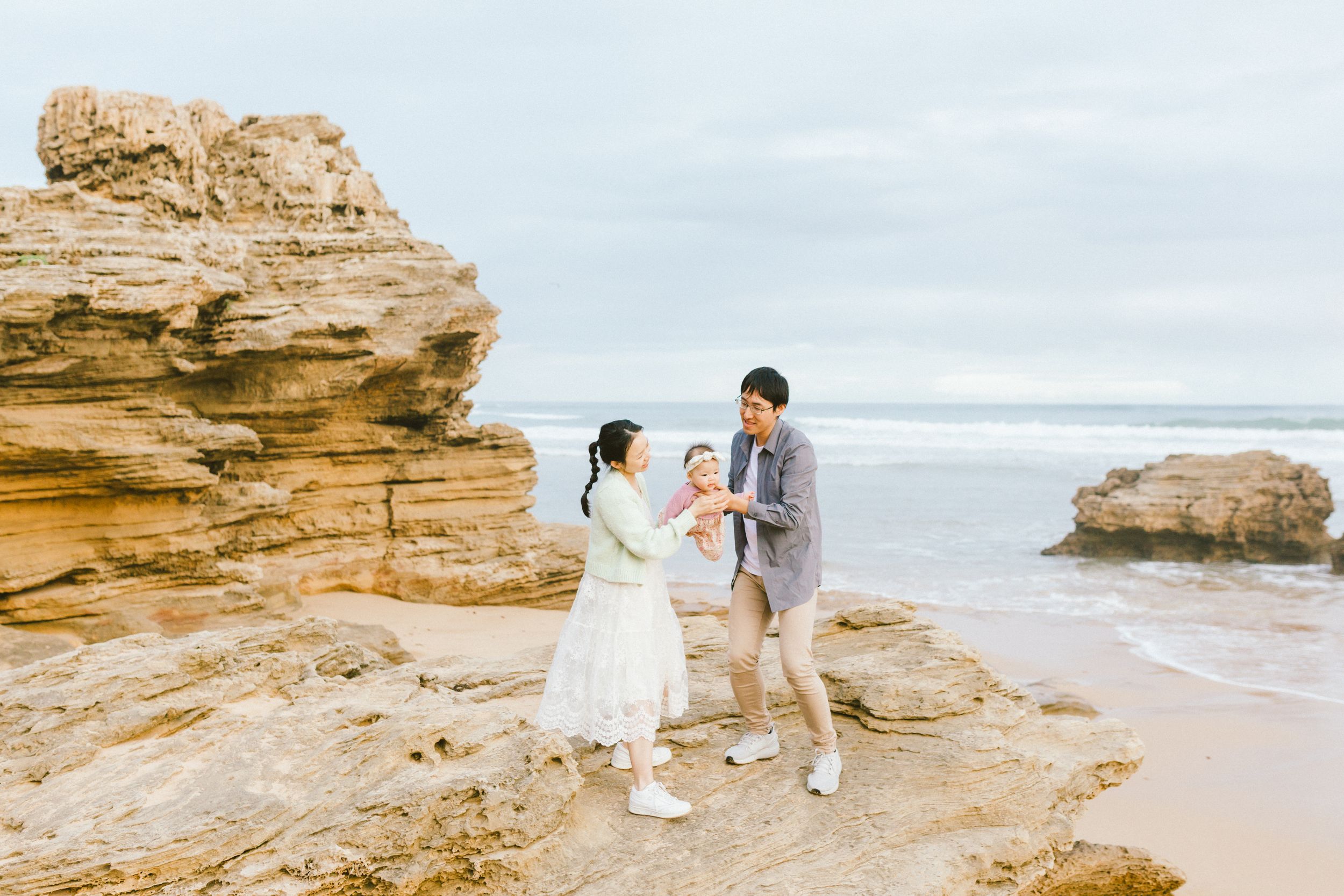 A couple walks along a scenic coastal beach with dramatic sandstone cliffs and ocean views at sunset.