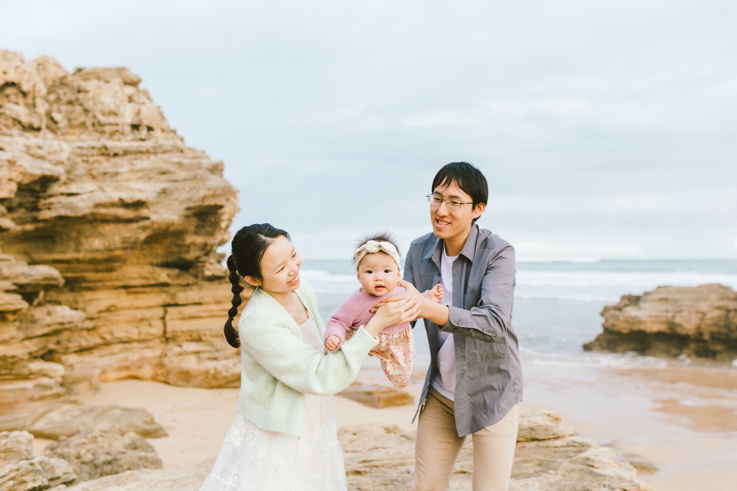 A couple shares tender moments on a rocky beach during sunset with ocean waves and cliffs in the background.