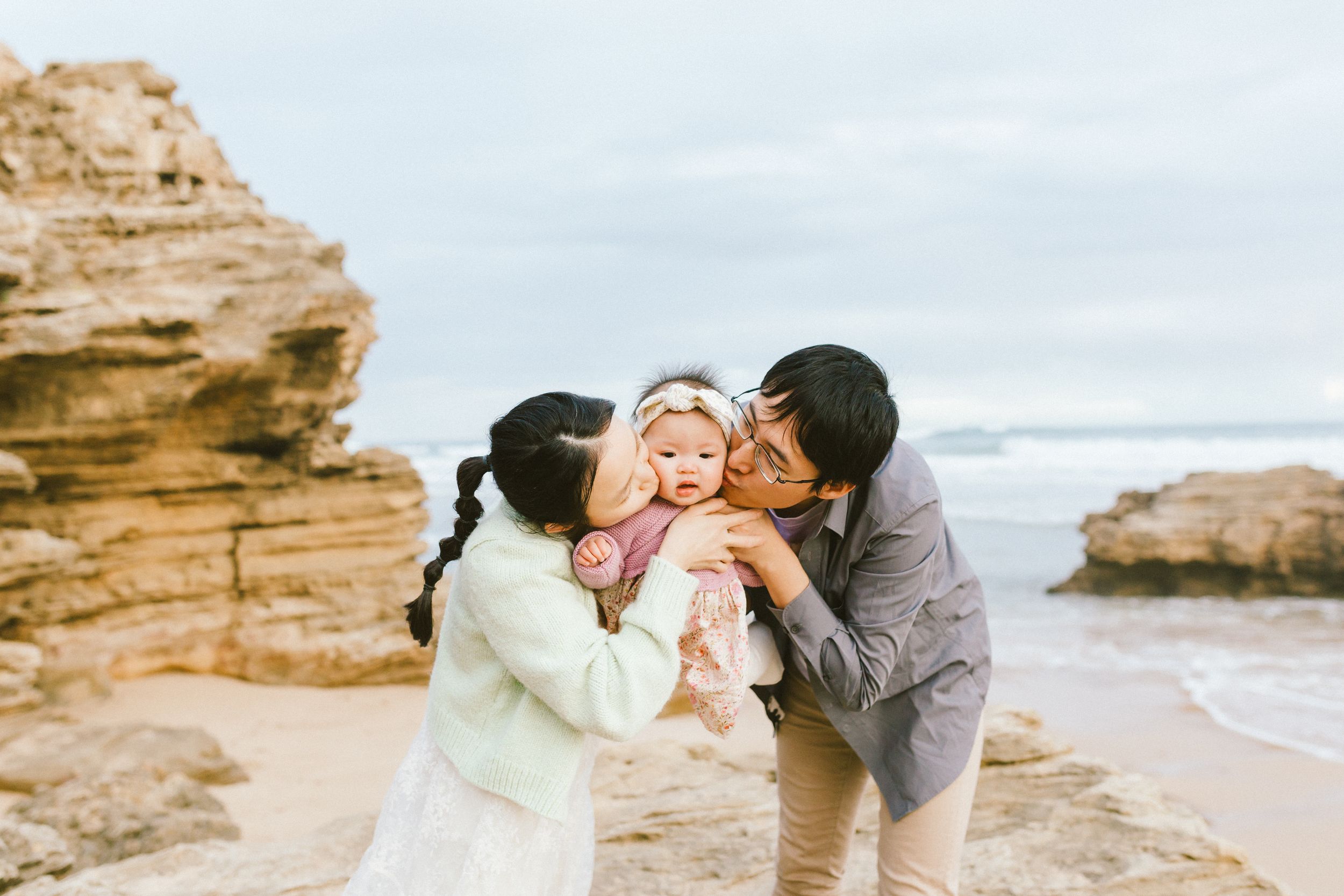 A couple shares romantic moments along a scenic beach with rocky cliffs and coastal views at sunset.