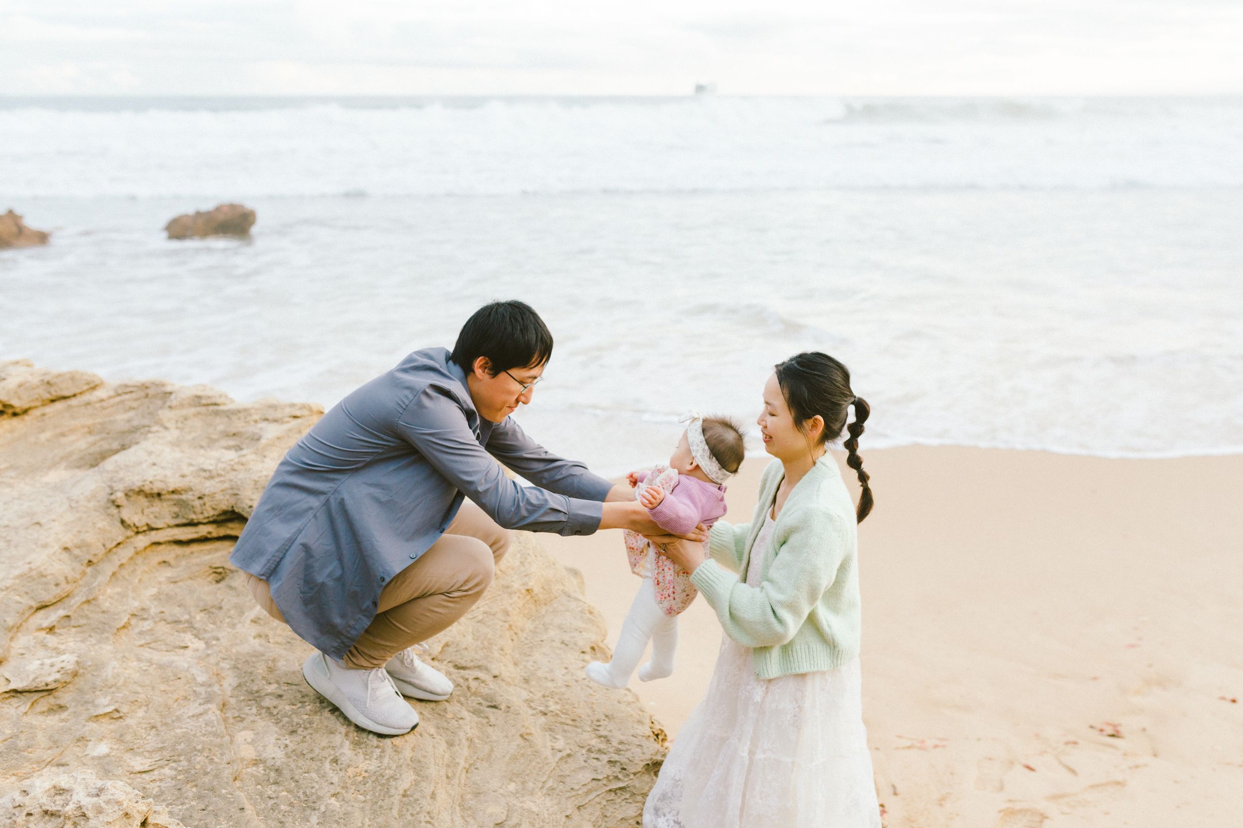 Family enjoying a tender moment together on a scenic beach with calm waters in the background.