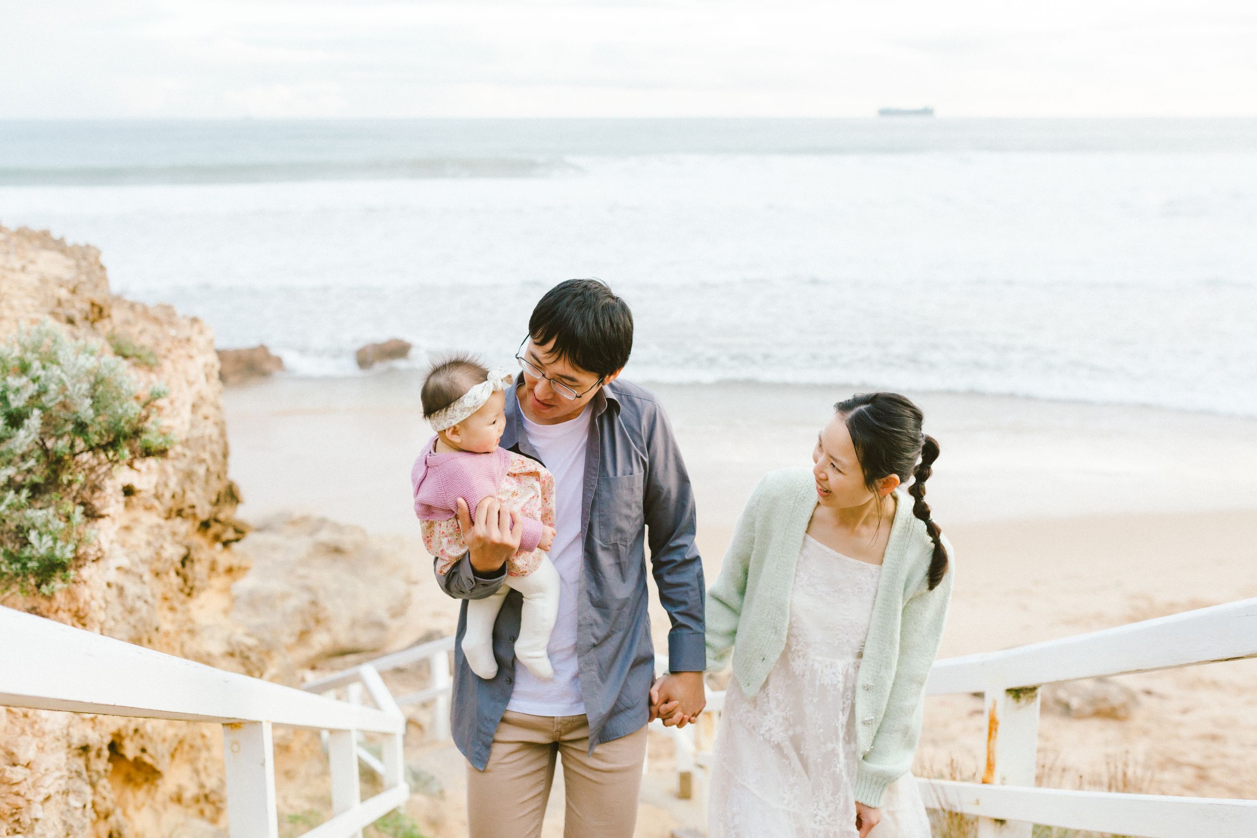 A family enjoying a scenic coastal view from a stairway overlook on a bright sunny day at the beach.