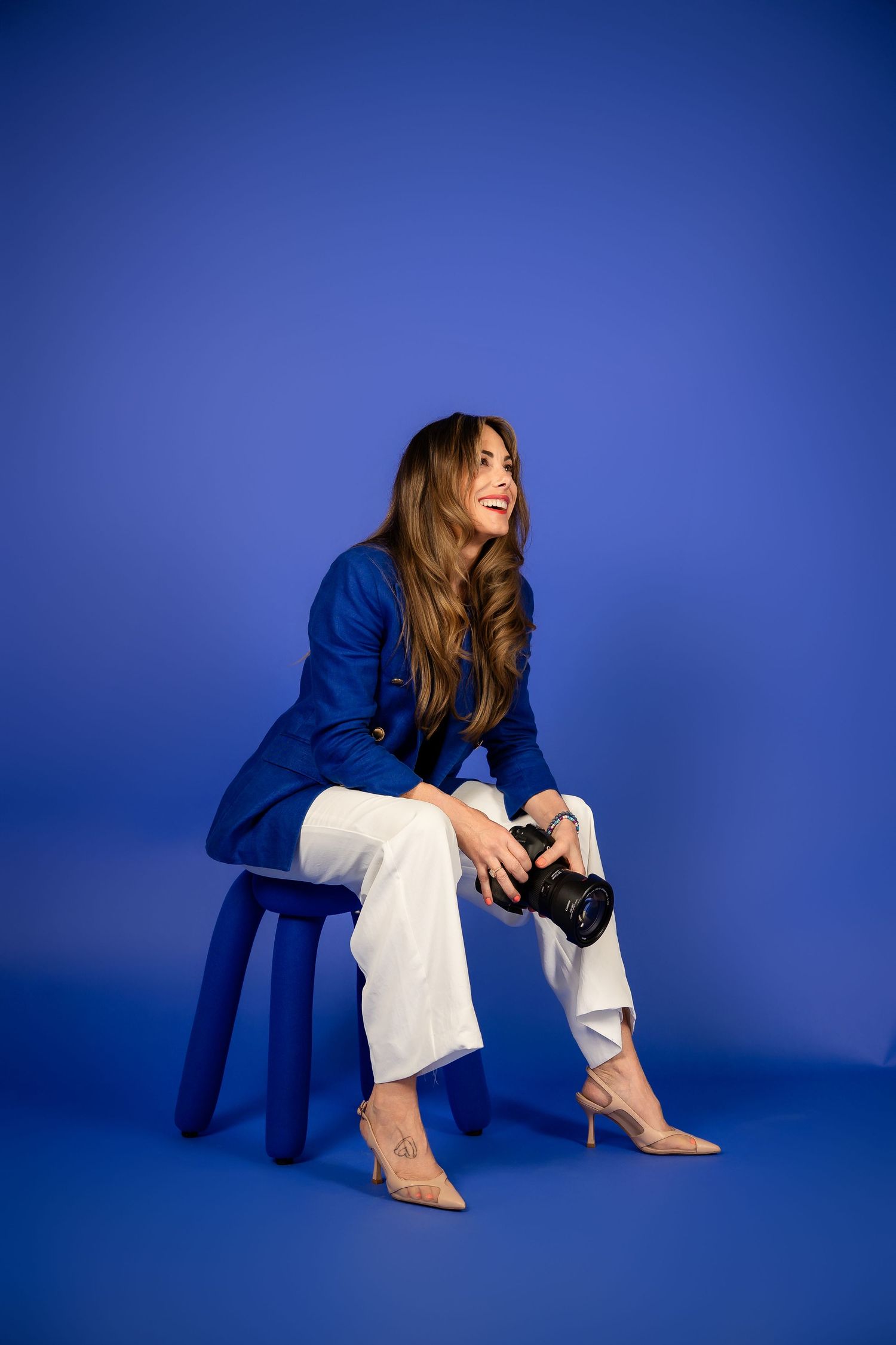 Person in a royal blue blazer and white top poses against a vibrant blue background with a warm smile.