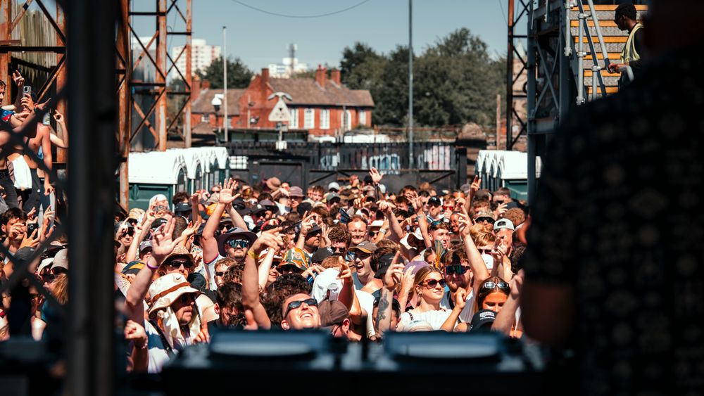 A large crowd of excited fans cheer and raise their arms during an outdoor wrestling or entertainment event.