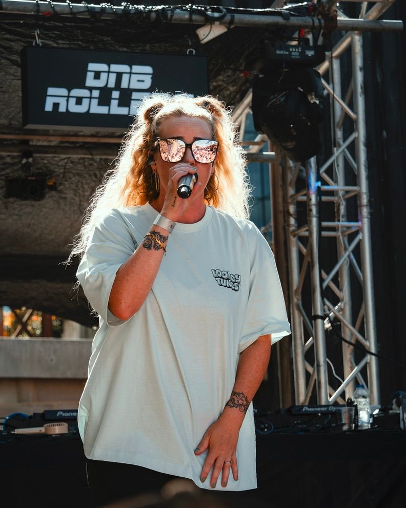 Performer in white t-shirt and sunglasses sings passionately on stage during live concert performance.