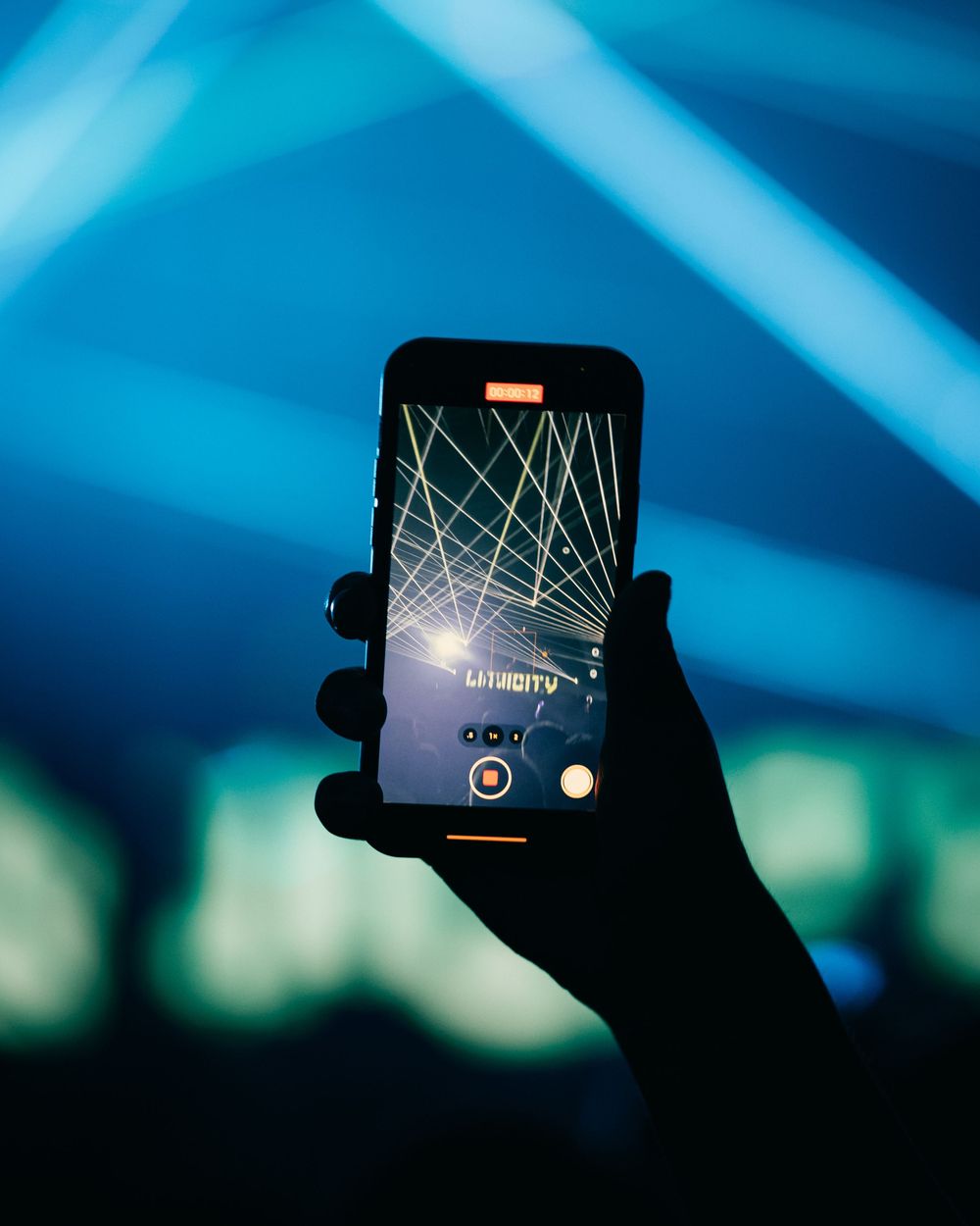 Silhouetted hands holding mobile phones against blue lighting at a concert or event.