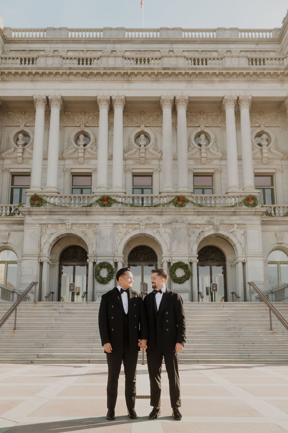 Three people in black suits stand on grand marble steps of a historic government building.