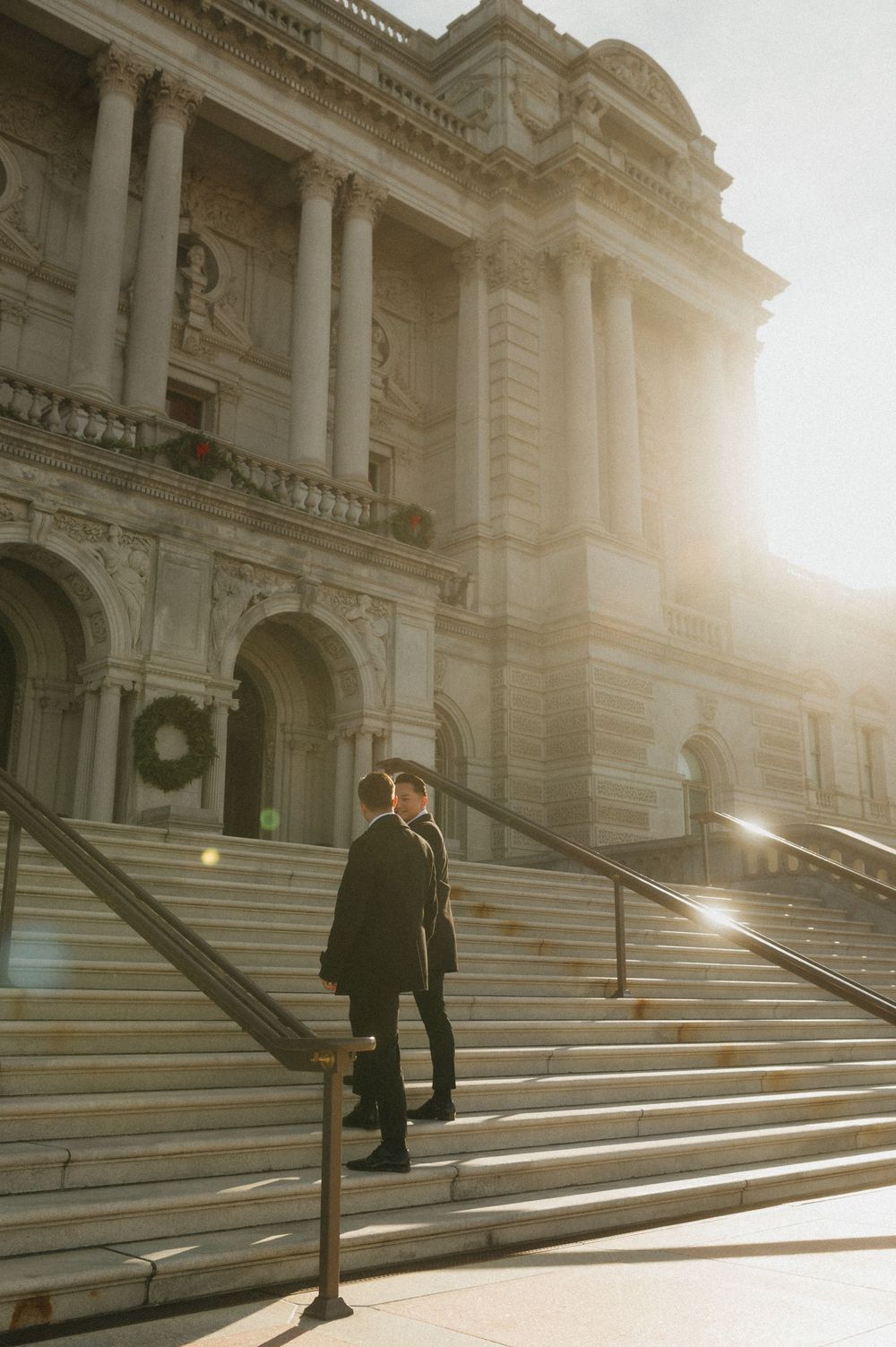 Person walking up grand stone steps of historic building with dramatic sunlight creating long shadows on architecture.