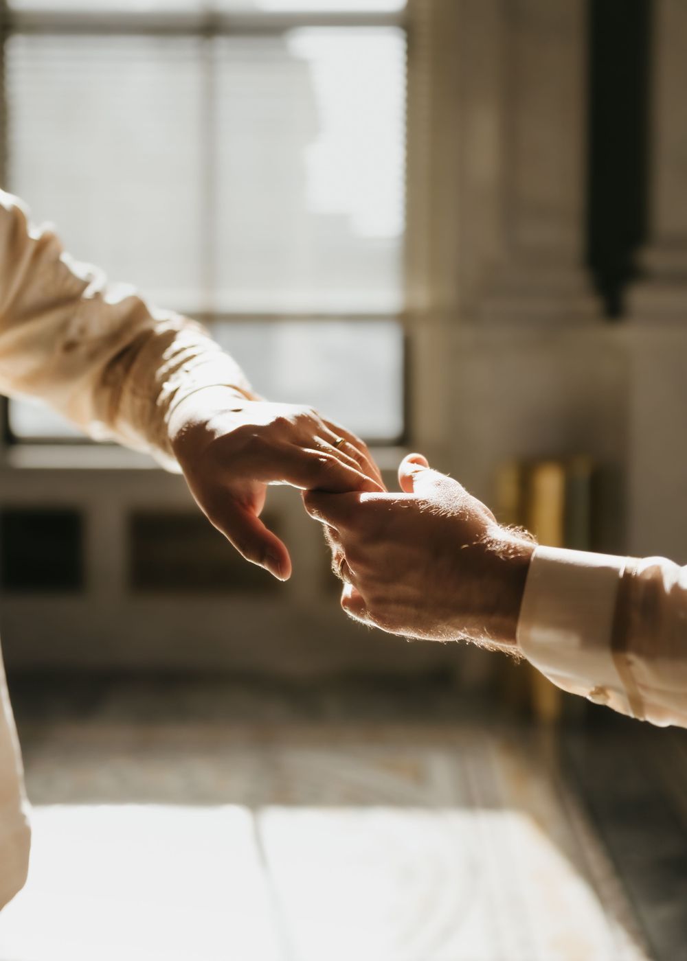 Hands reaching toward each other in a sunlit marble interior, creating a dramatic silhouette effect.