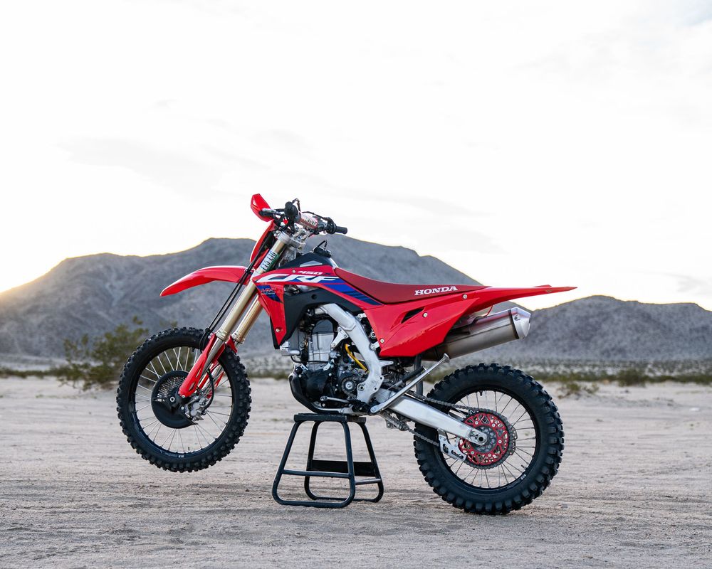 Red Honda CRF dirt bike displayed on a stand in a desert landscape with mountains in the background.