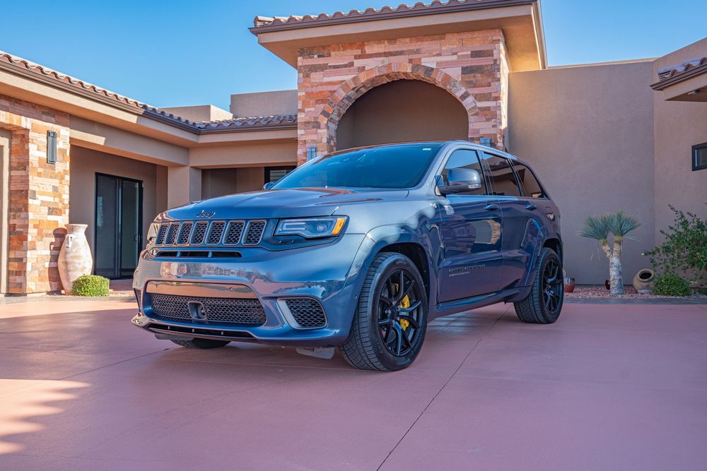 Gray Jeep Grand Cherokee Trackhawk SUV parked in front of a stone and stucco home with arched entryway.