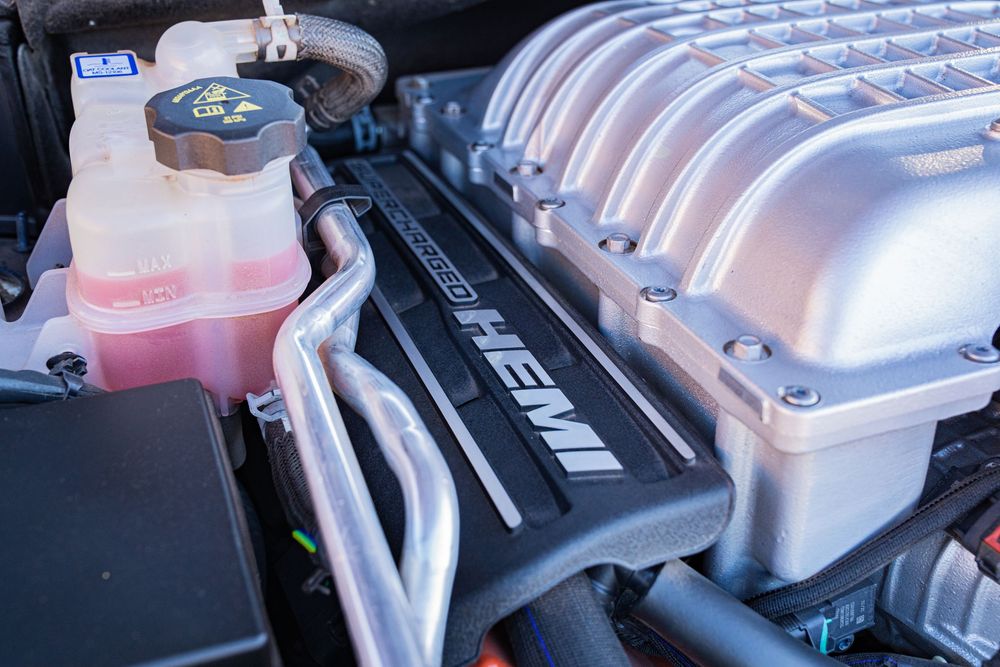 Close-up of a HEMI engine with supercharger and pink coolant reservoir in a high-performance vehicle engine bay.