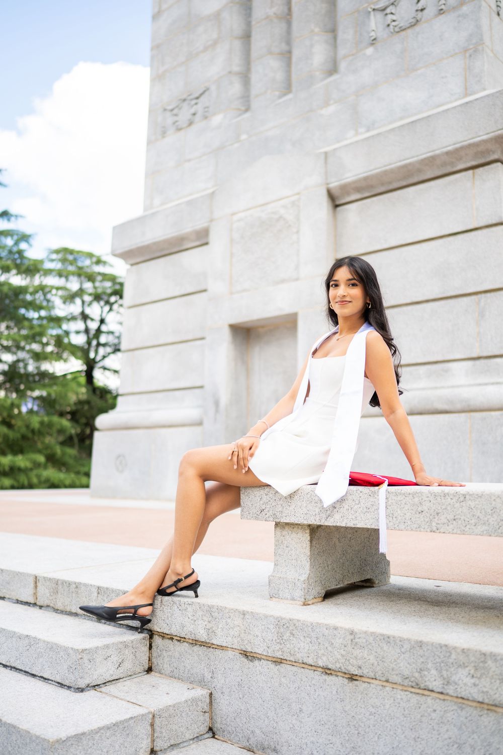 A white dress and red sash create an elegant contrast against stone steps in an outdoor portrait session.