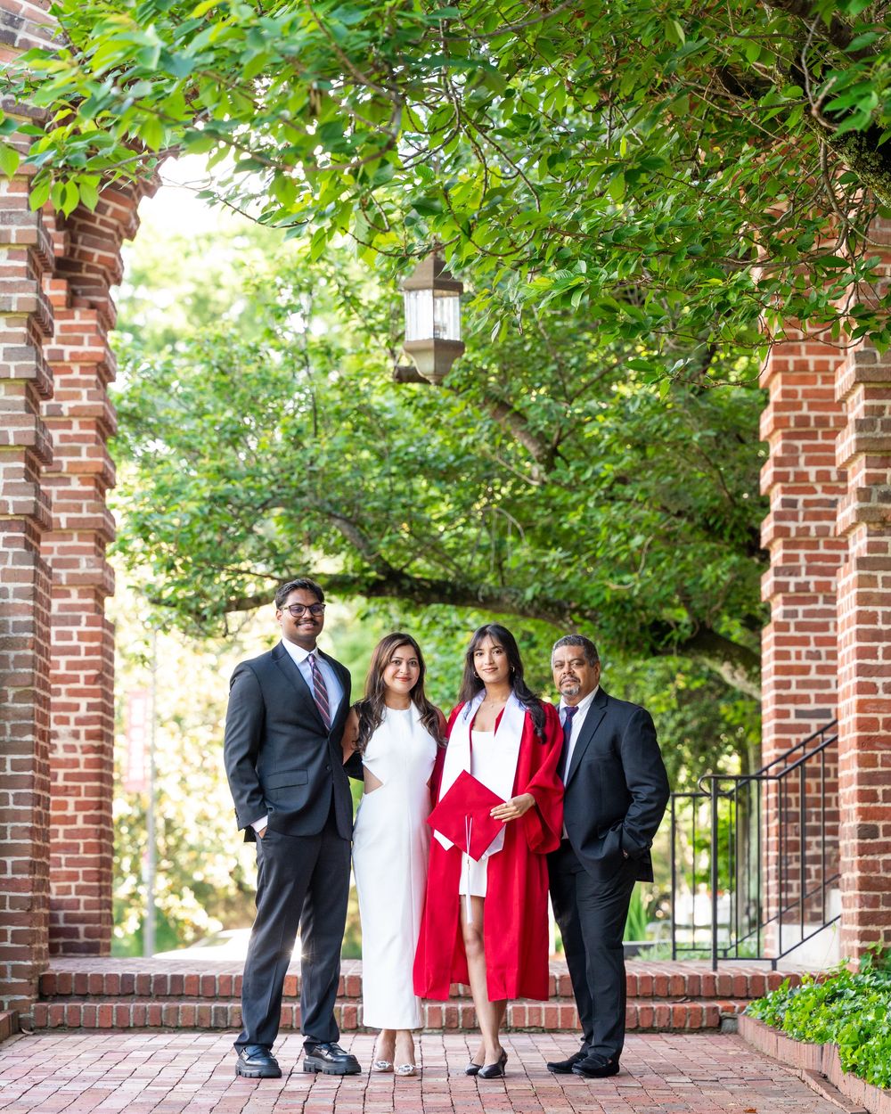 A group poses together under a brick archway surrounded by lush greenery on a sunny day.