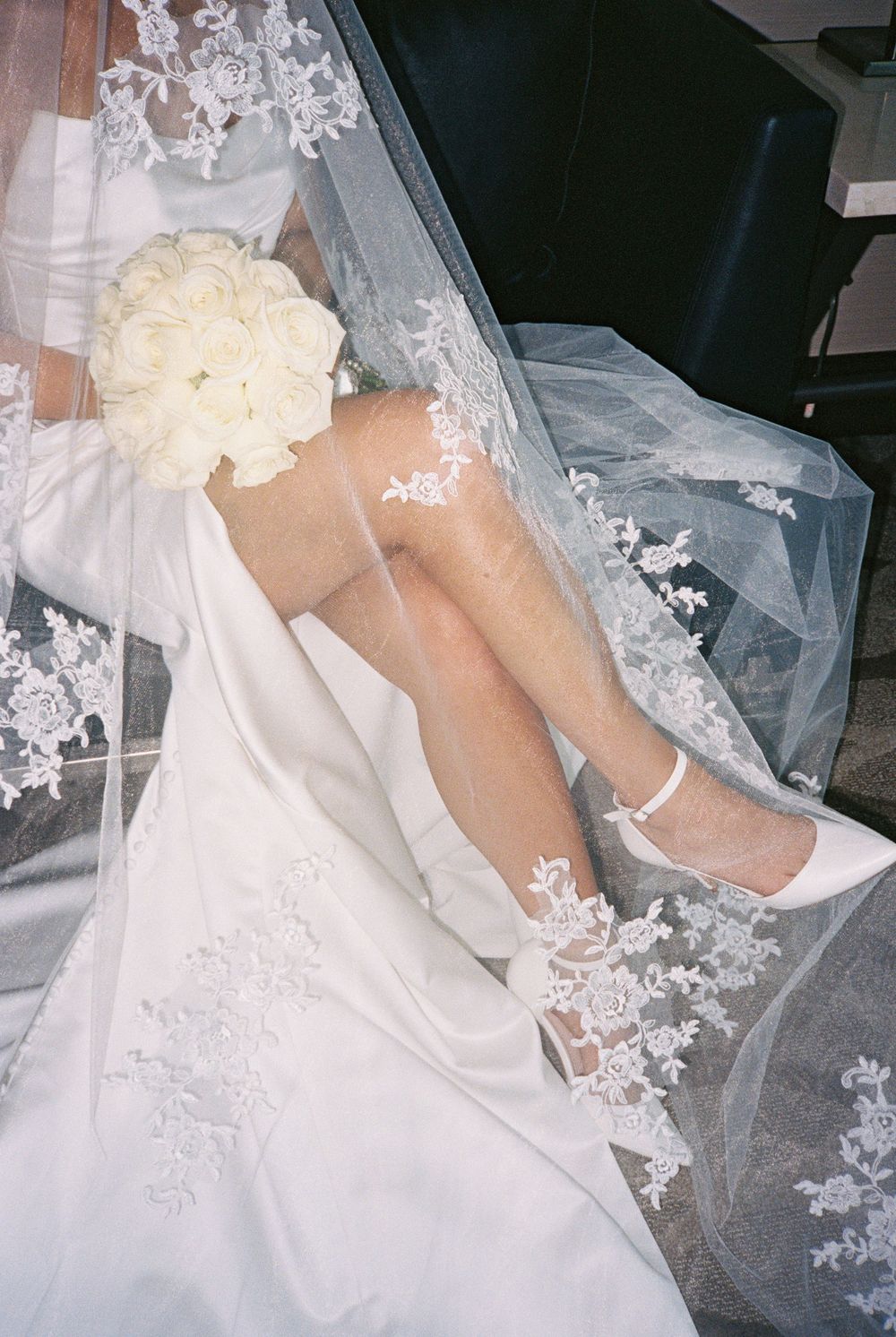 Bride in white lace wedding dress and veil, holding white rose bouquet, wearing white heels with ankle strap.