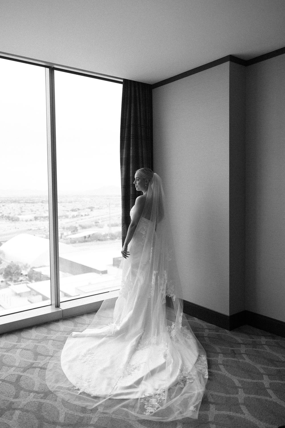 Dramatic black and white photos of a wedding dress with flowing train against large windows.
