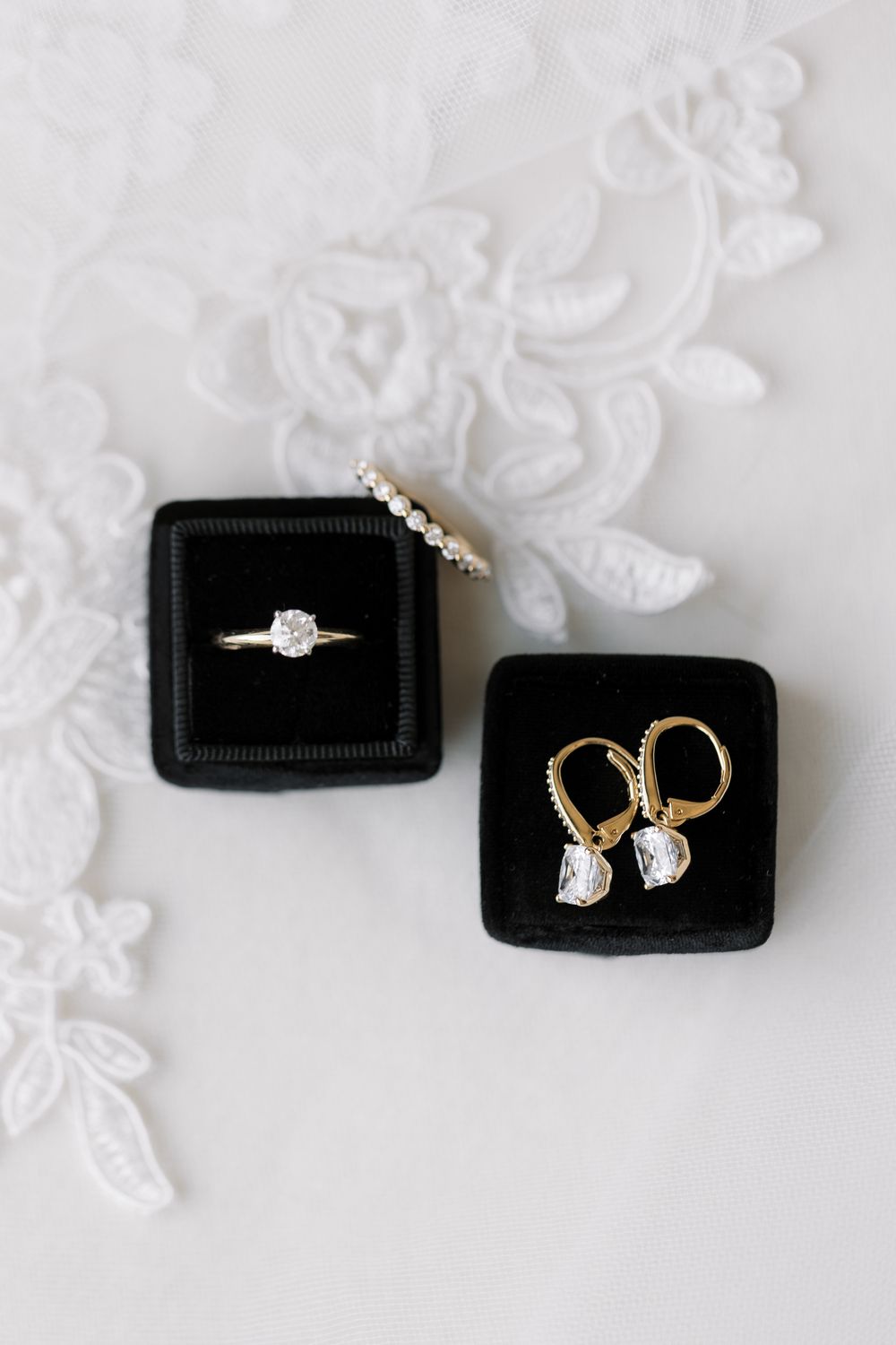 Elegant diamond jewelry including rings and earrings displayed on black velvet boxes with white floral background.