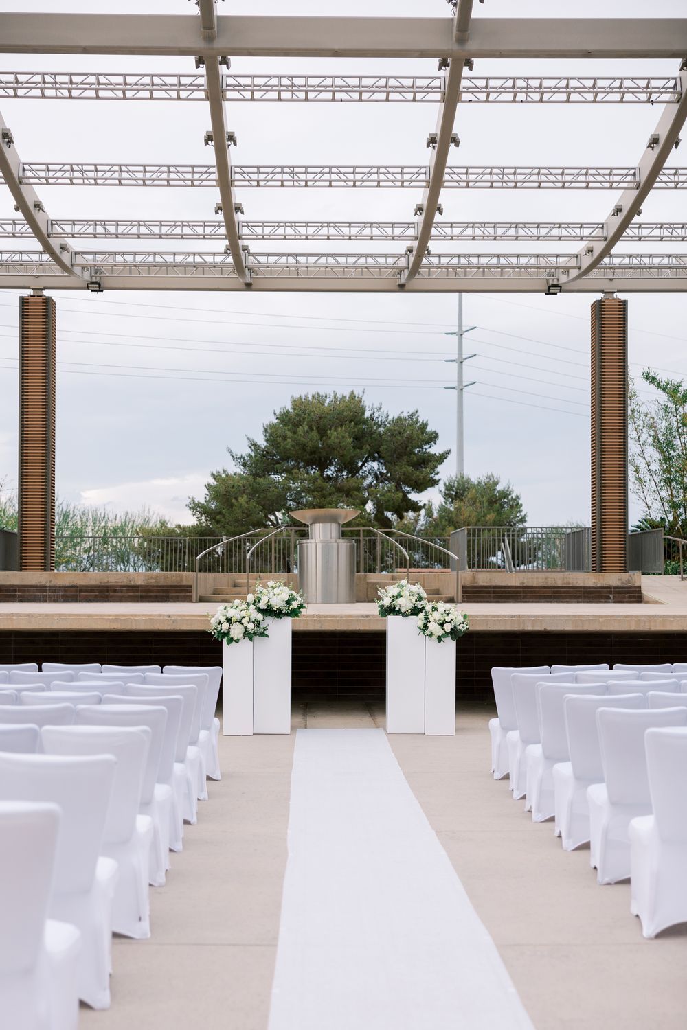 White chairs arranged in rows for an outdoor wedding ceremony under a modern covered venue with floral decorations.