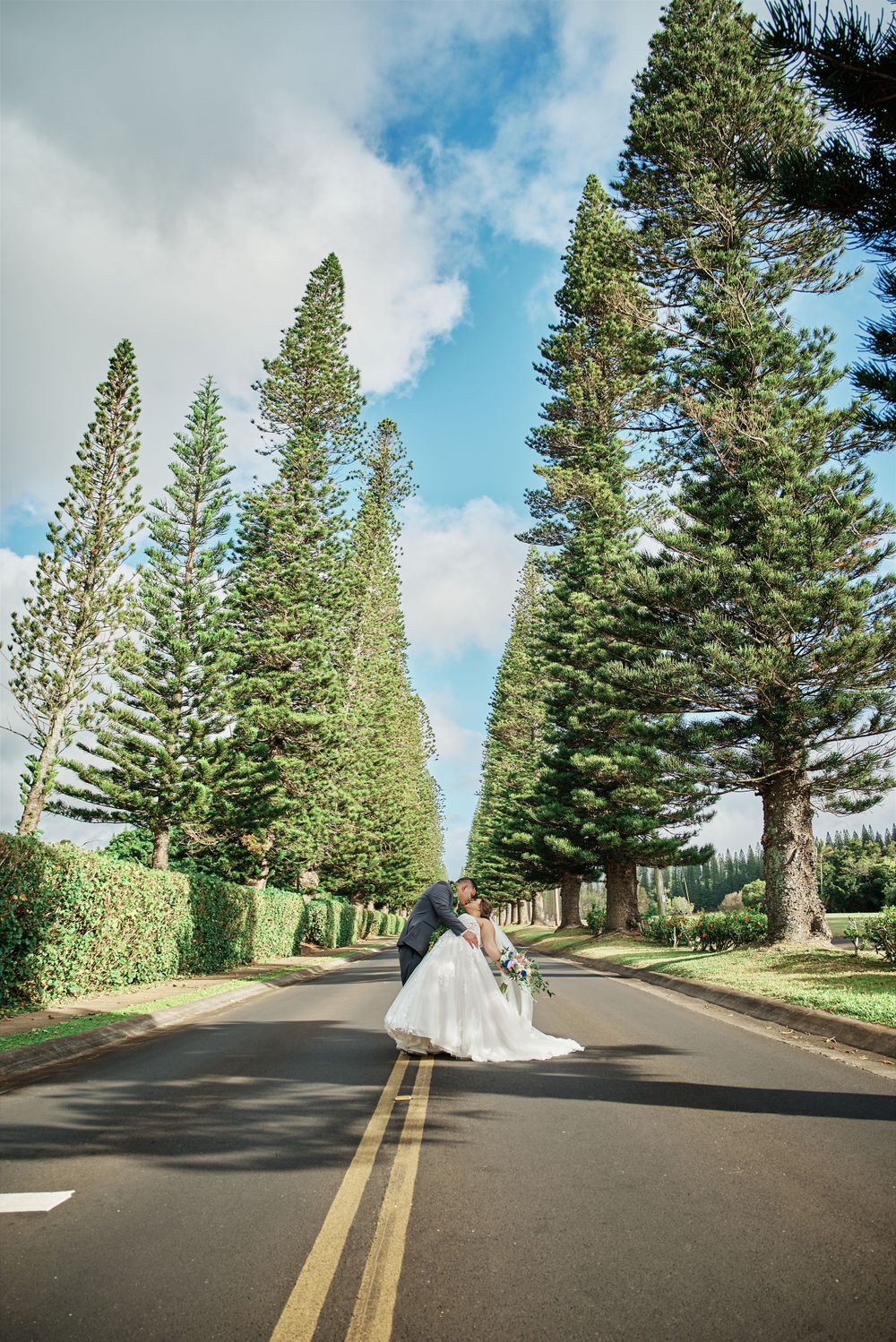 Wedding couple poses on a tree-lined road for dramatic wedding photography sequence.
