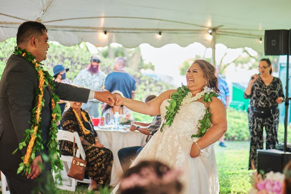 A couple wearing traditional Hawaiian leis dances at their wedding reception under a white tent.