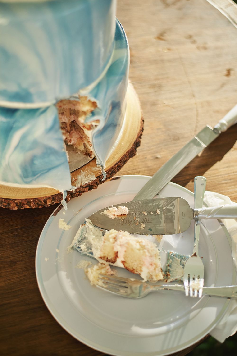 A partially eaten slice of wedding cake with blue frosting on a white plate.