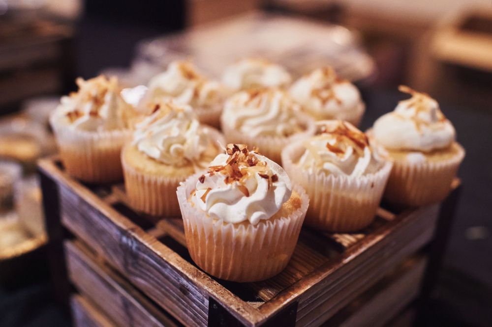 Frosted cupcakes with sprinkles displayed in a wooden box at a wedding dessert table.