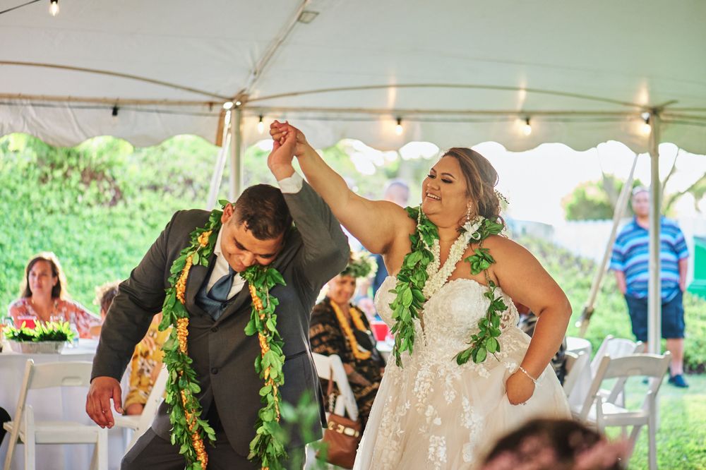 A couple dances joyfully during their wedding reception wearing green leis.
