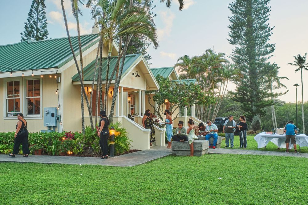 Wedding guests gather outside a charming tropical venue with palm trees and green landscaping.