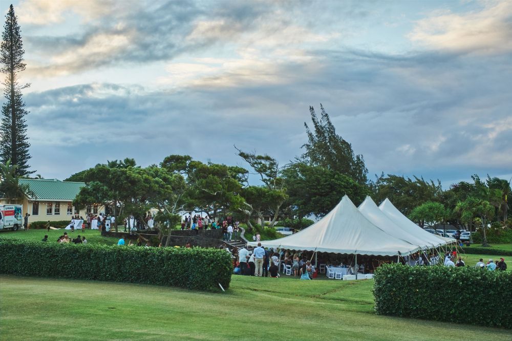 An outdoor wedding reception with white tents set up on a lush green lawn at sunset.