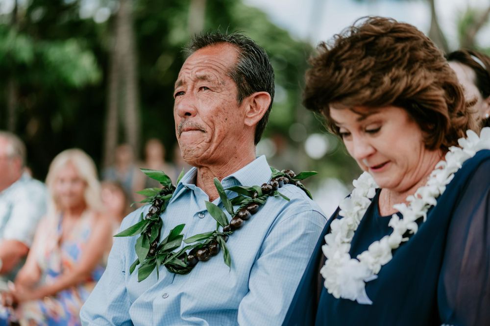 Guests observe a wedding ceremony from white chairs in a tropical outdoor setting.