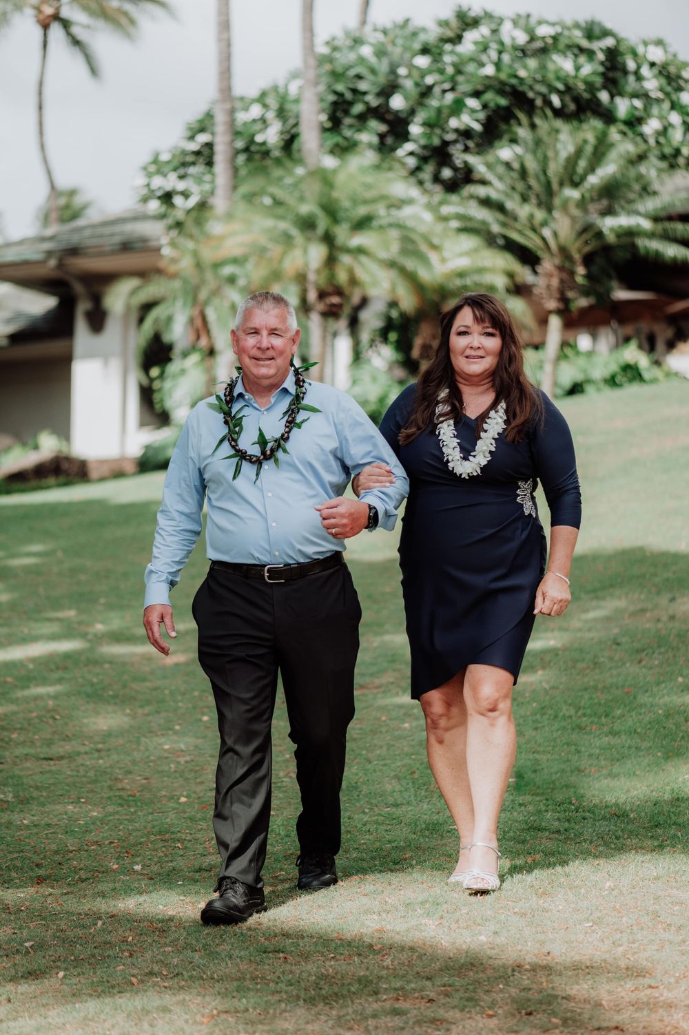 Wedding party members walk along a garden path surrounded by tropical plants.
