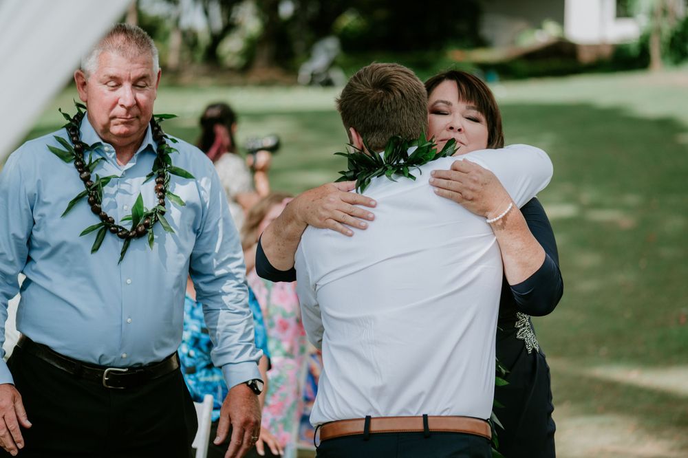 Wedding guests embrace during outdoor celebration on grassy lawn.