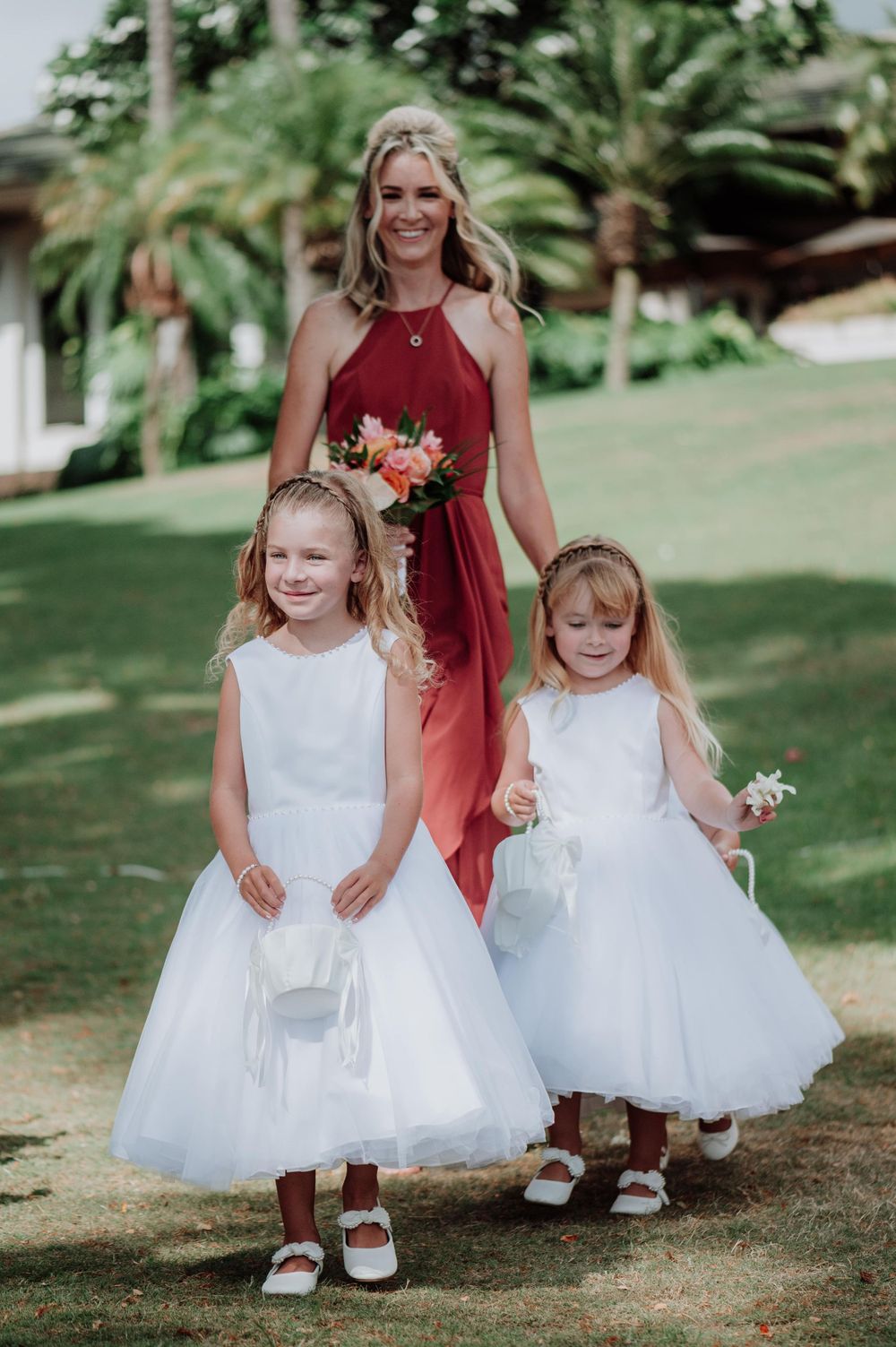 Flower girls in white tulle dresses walk down grassy aisle at outdoor wedding.