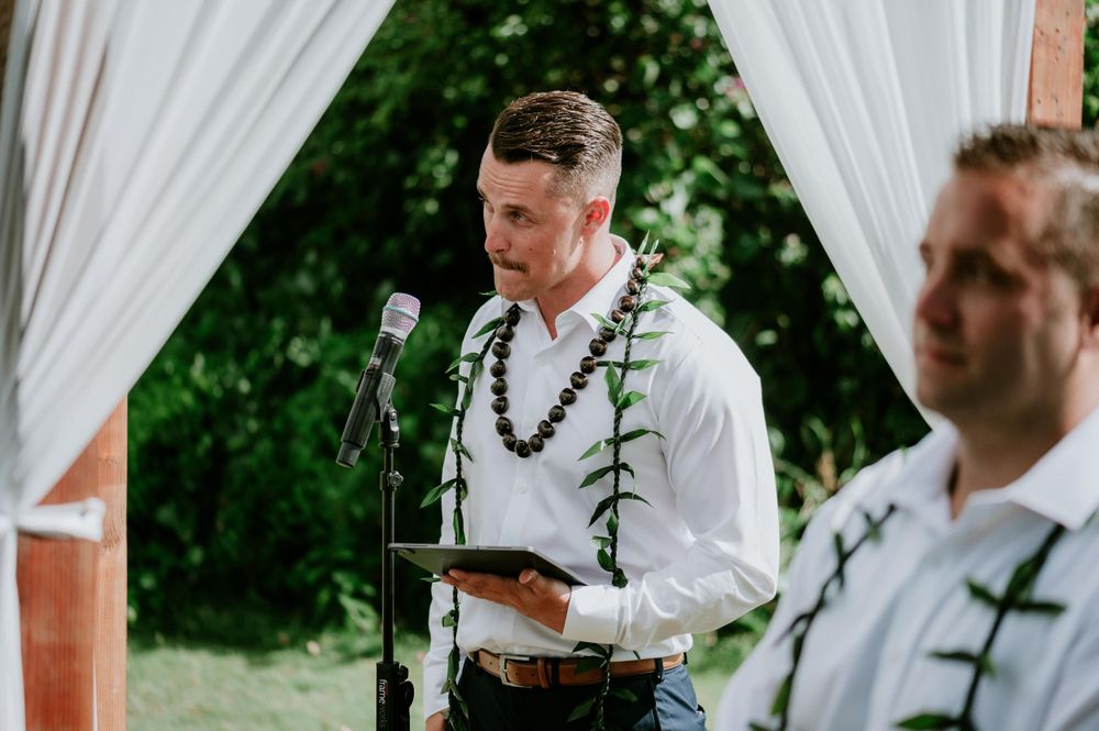 Wedding ceremony in progress under white draped arbor with tropical greenery.