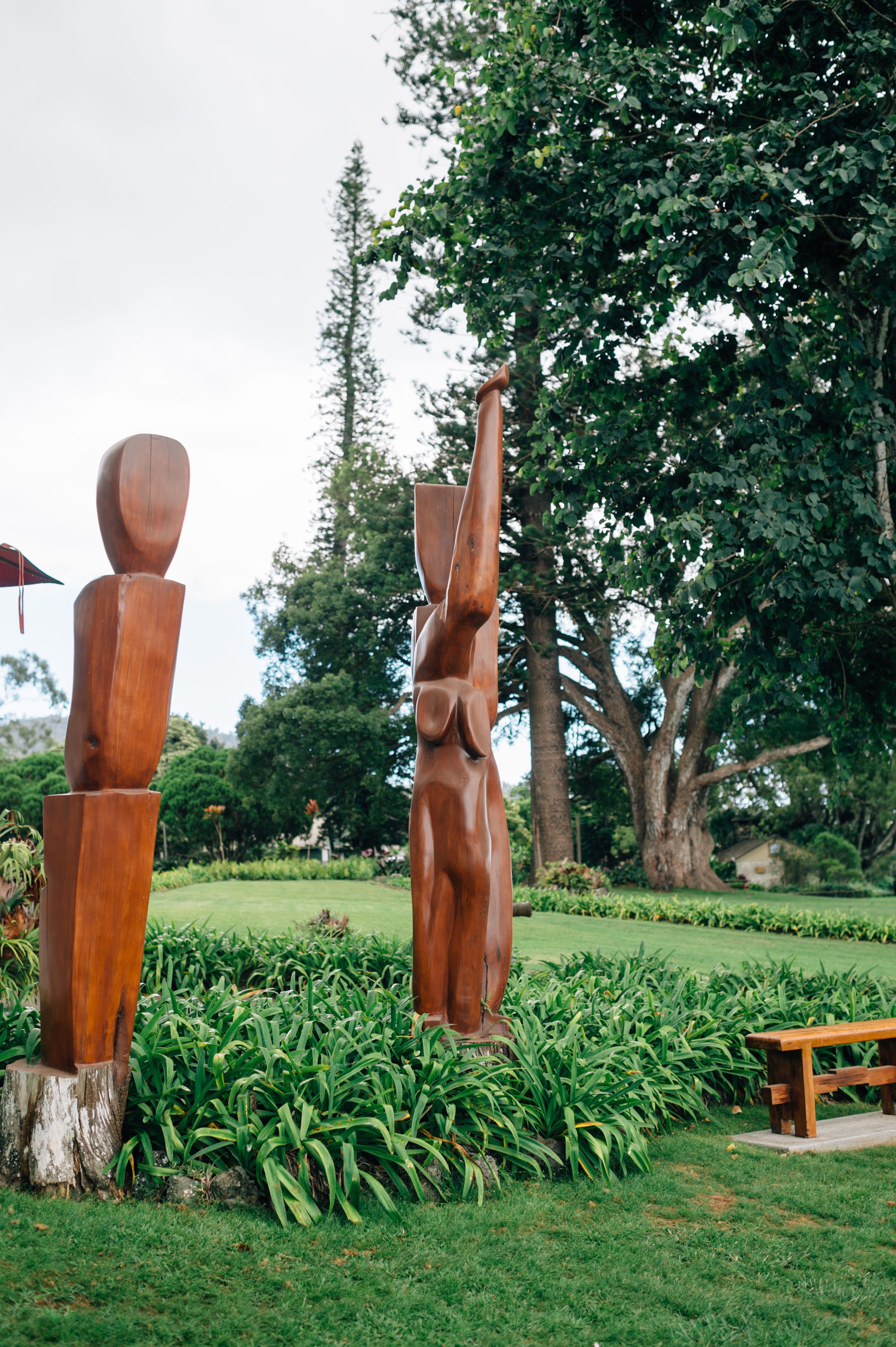 Wooden carved sculptures displayed in a grassy garden setting with trees in the background.