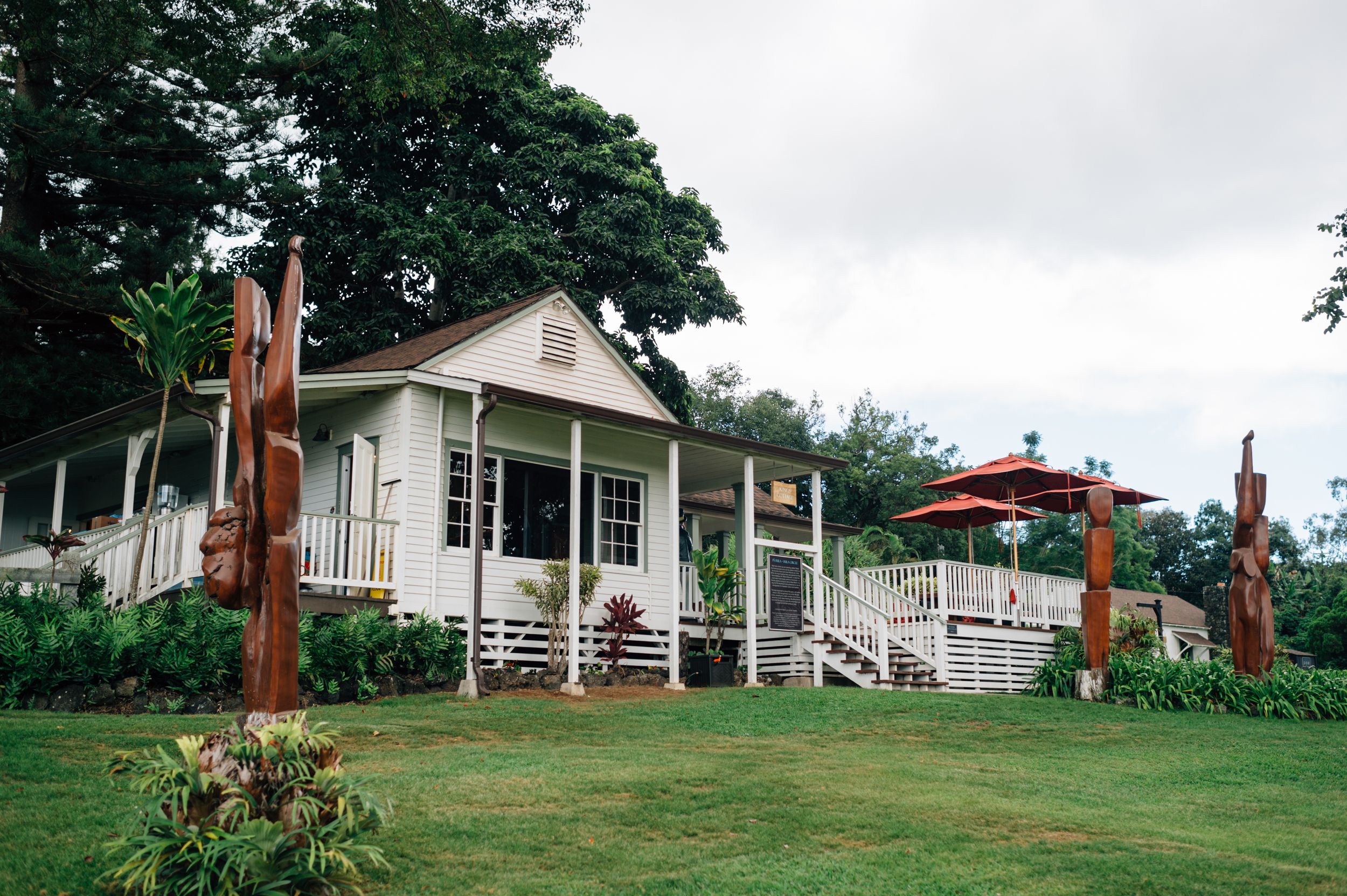 White cottage-style buildings nestled among trees with wooden sculptures in the landscaped yard.