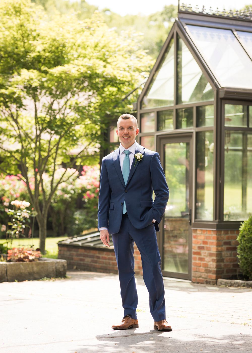 Dapper groom in navy blue suit with mint tie poses outdoors before wedding ceremony.