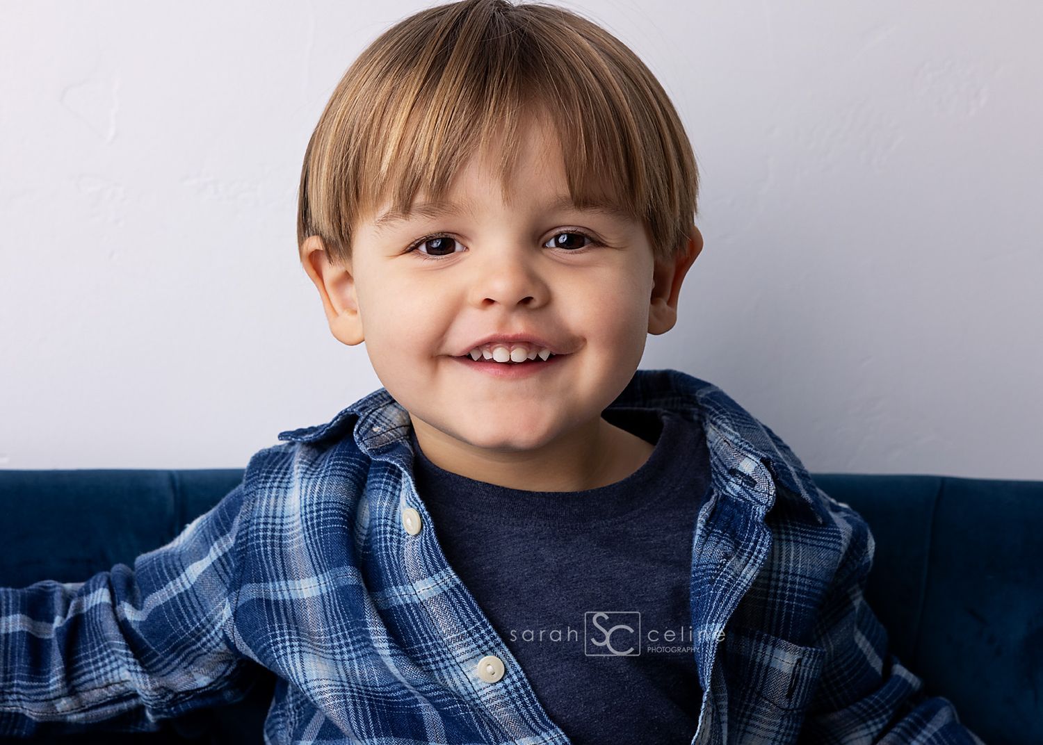A young child wearing a blue plaid shirt smiles brightly in a series of five connected portrait photos.