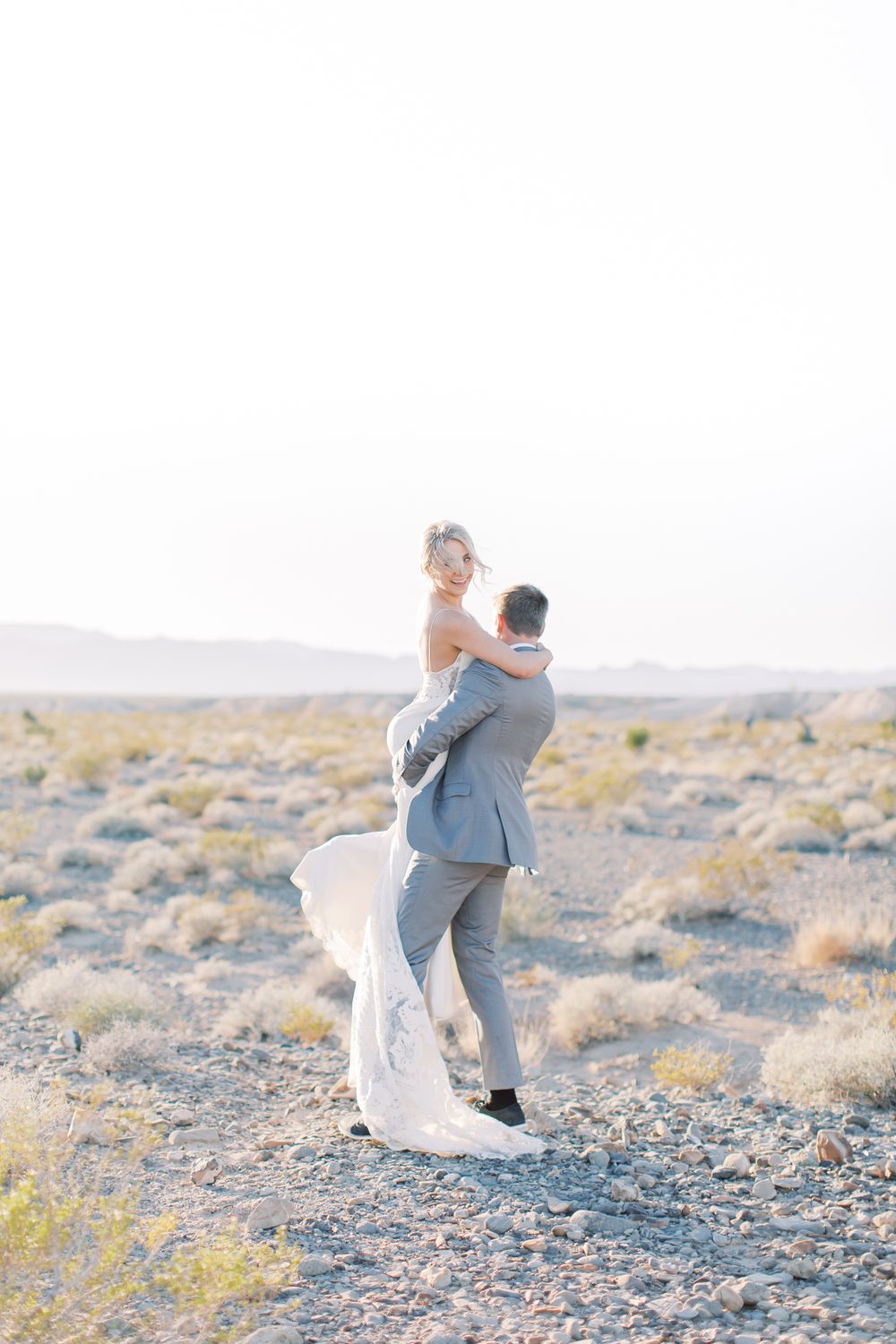 A romantic desert wedding photo of a couple embracing against a desert landscape at sunset.