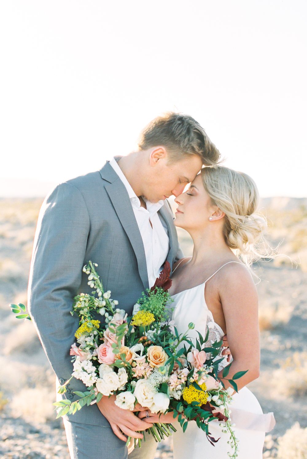A tender moment between newlyweds with a beautiful wildflower bouquet in the desert.
