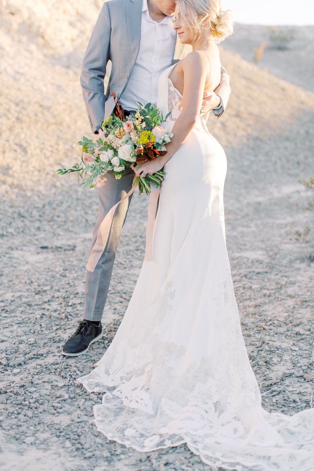 Wedding couple walking together with bride holding a colorful bouquet against desert backdrop.