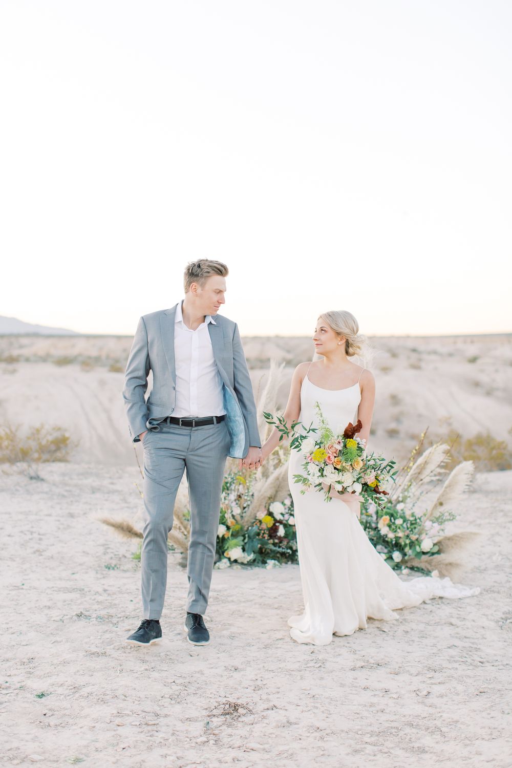 Romantic desert wedding portraits featuring a couple in grey and white attire with natural desert scenery.