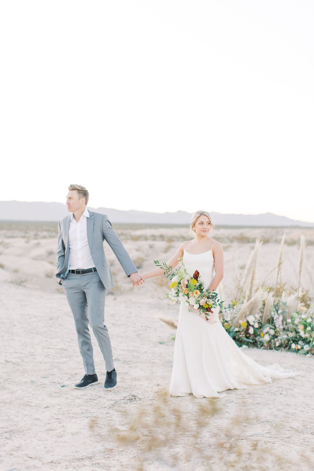Wedding couple posing in desert setting with floral decorations on sandy ground.