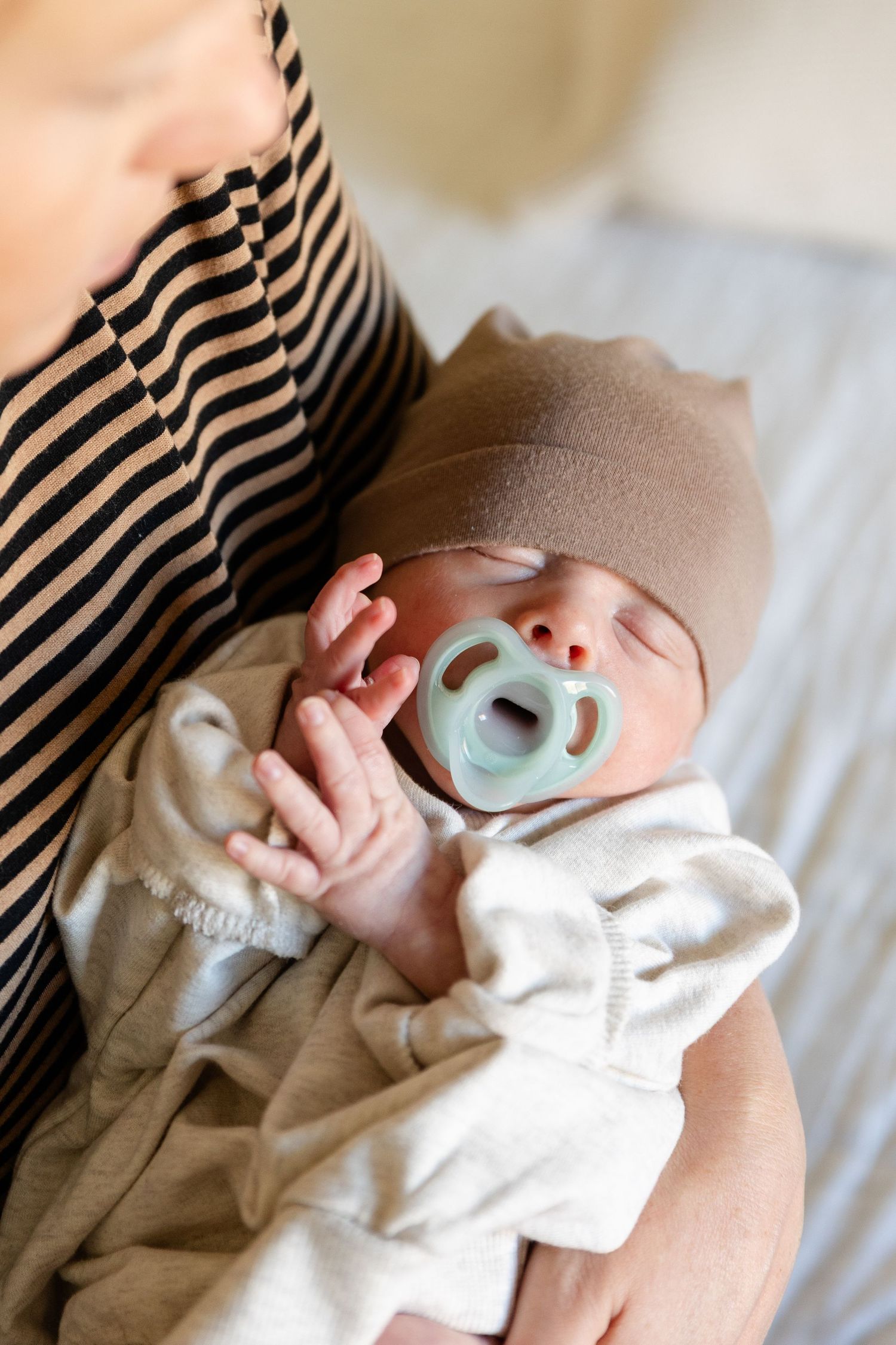 mom holding baby in oversized shirt beanie and binky southern utah newborns photography