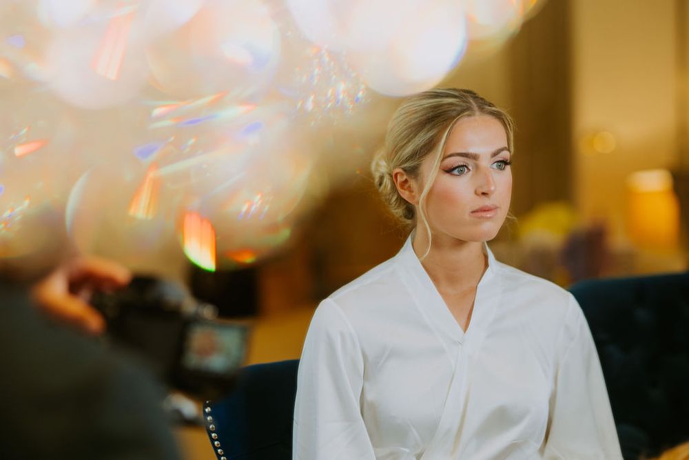 A person in a white robe sits with a contemplative expression while soft golden lights blur in the background.