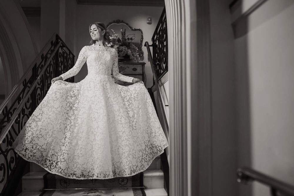 A bride in a white lace wedding dress twirls gracefully in a room, showing off the full skirt's movement.