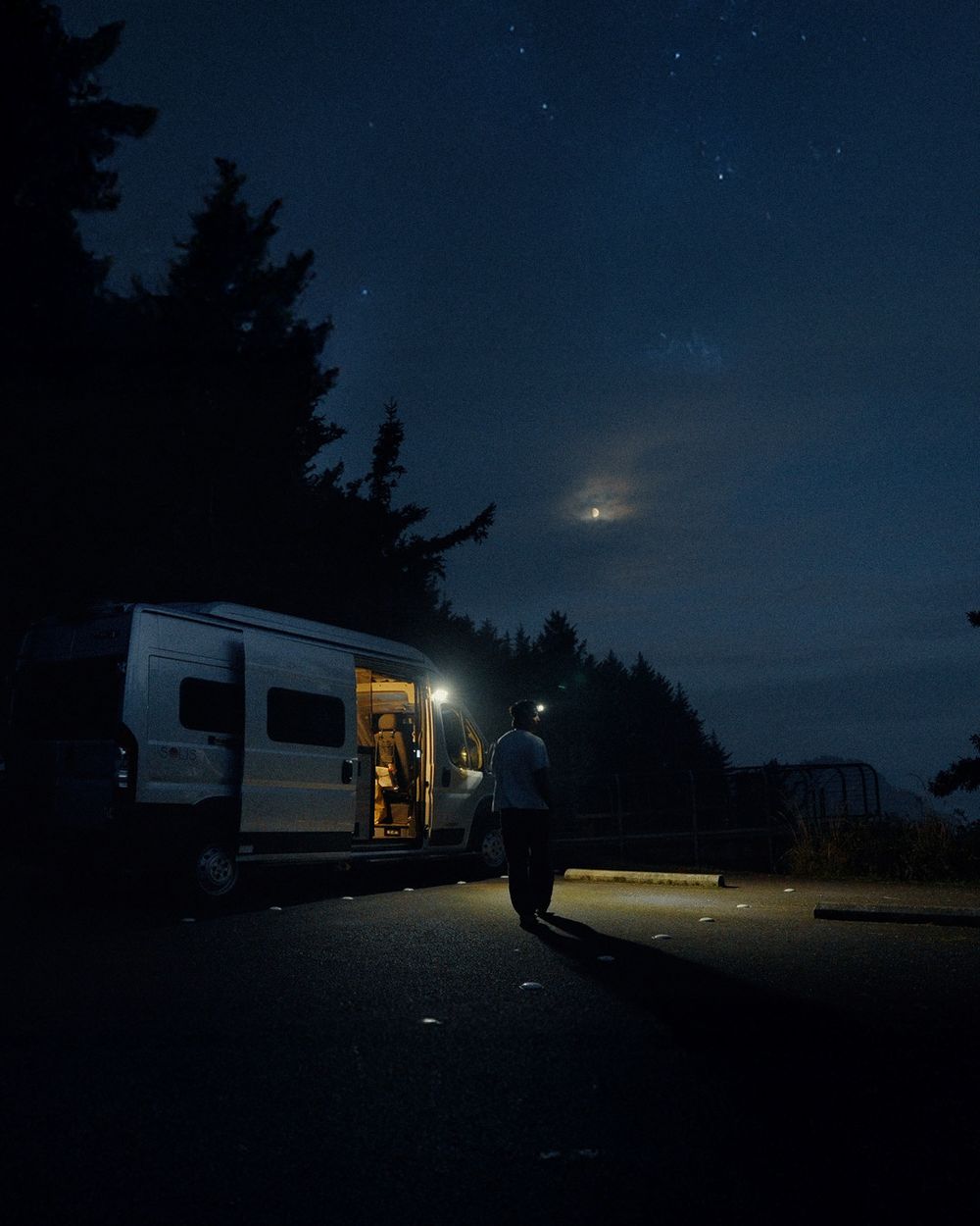 Nighttime camping scene with illuminated RVs under a starry sky in the forest.