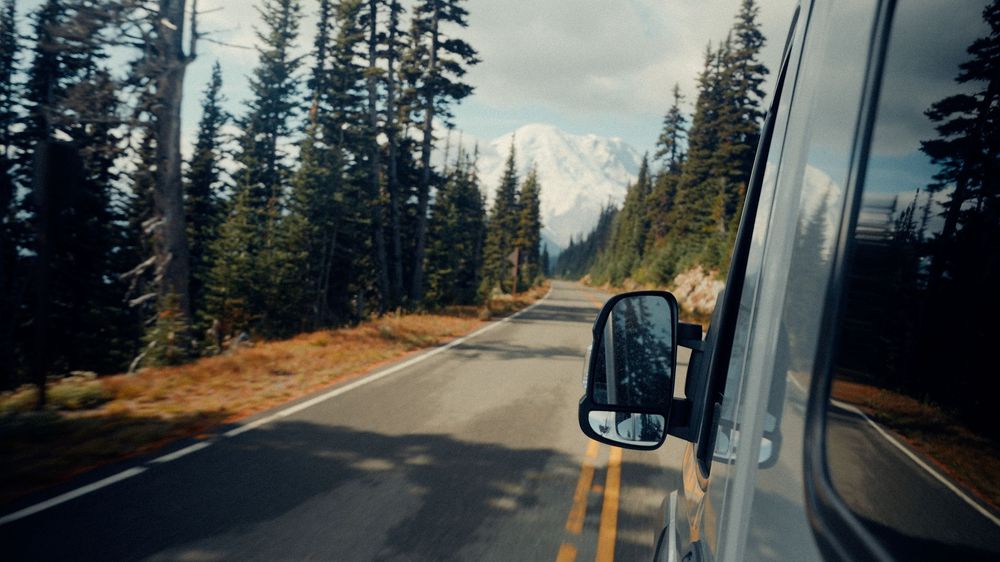 Panoramic view of a mountain highway winding through evergreen forests under cloudy skies.