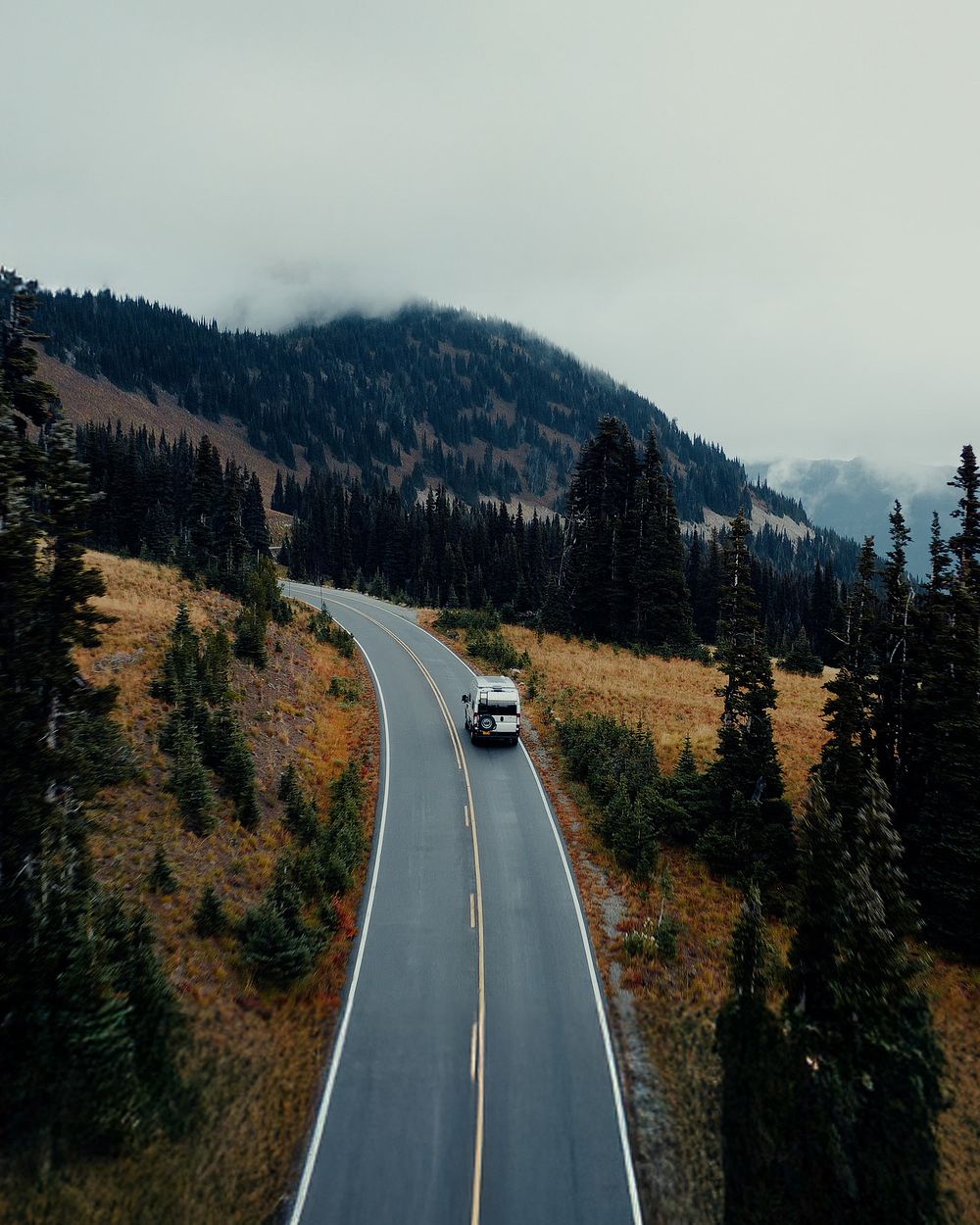 Aerial view of a curved mountain road with vehicles traveling through autumn terrain.