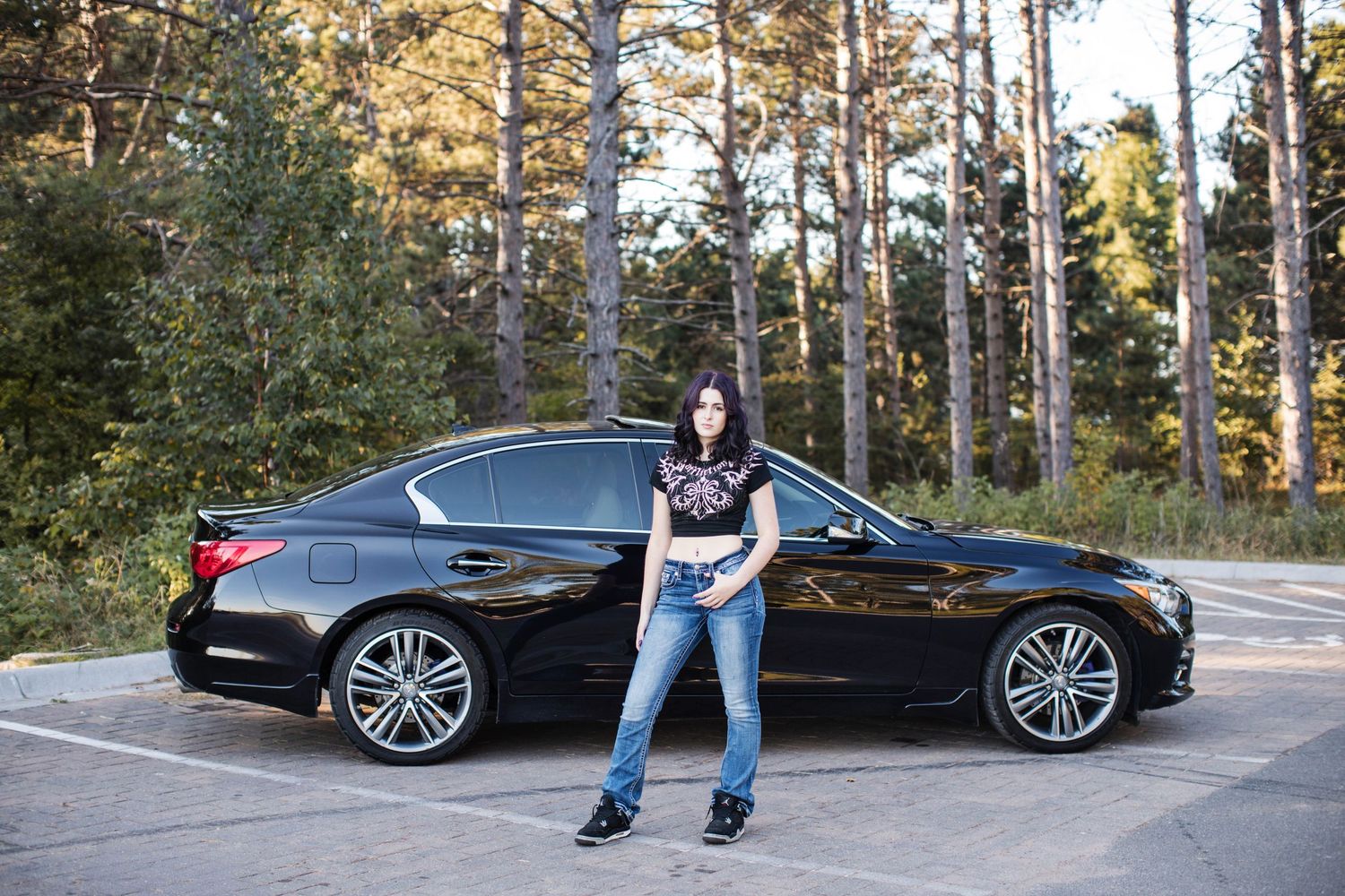 A black luxury car parked in a wooded area with pine trees in the background.