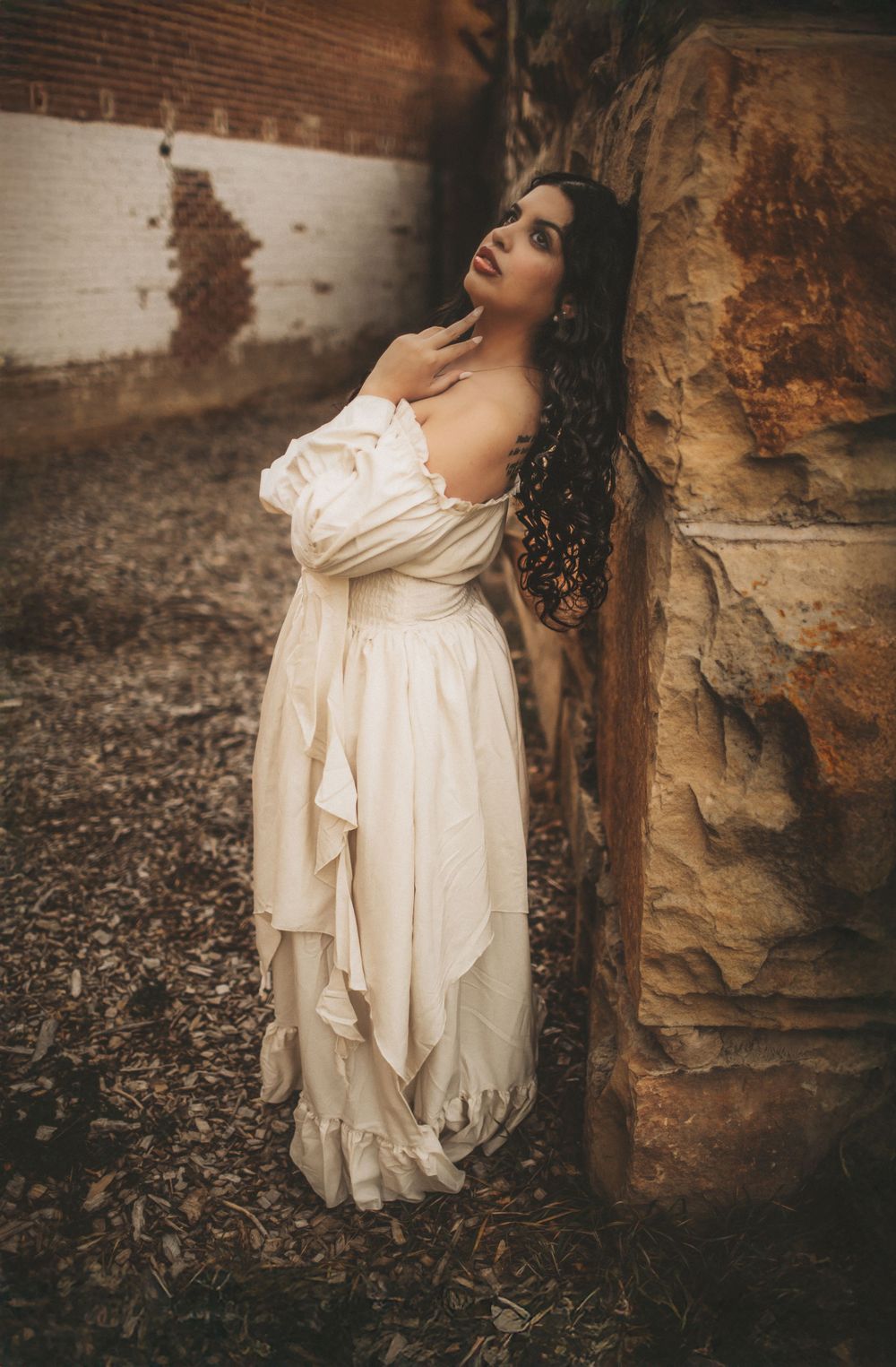 Full body cinematic portrait of a woman in a flowing dress standing against natural rock textures, captured in a moody storytelling style